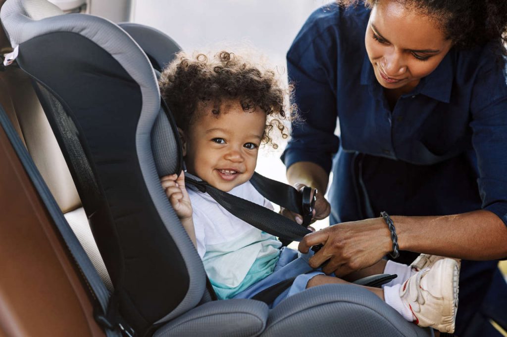 mãe coloca o cinto de segurança em seu filho na cadeirinha de carro